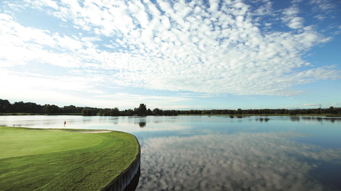Eine ruhige Landschaft mit einem weitläufigen See und einem grünen Golfplatz. Der Himmel ist mit schönen, lockeren Wolken bedeckt. | © GV Murstätten
