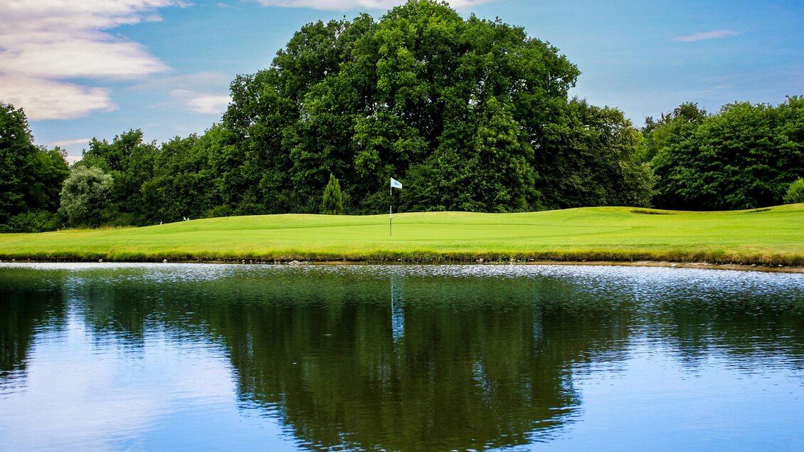 Green mit Fahne und Wasserhindernis im Golfclub Grazer MurAuen, mit Spiegelung der Bäume im Wasser in Gössendorf.  | © Golferlebnis Steiermark - Manuel Wiedner