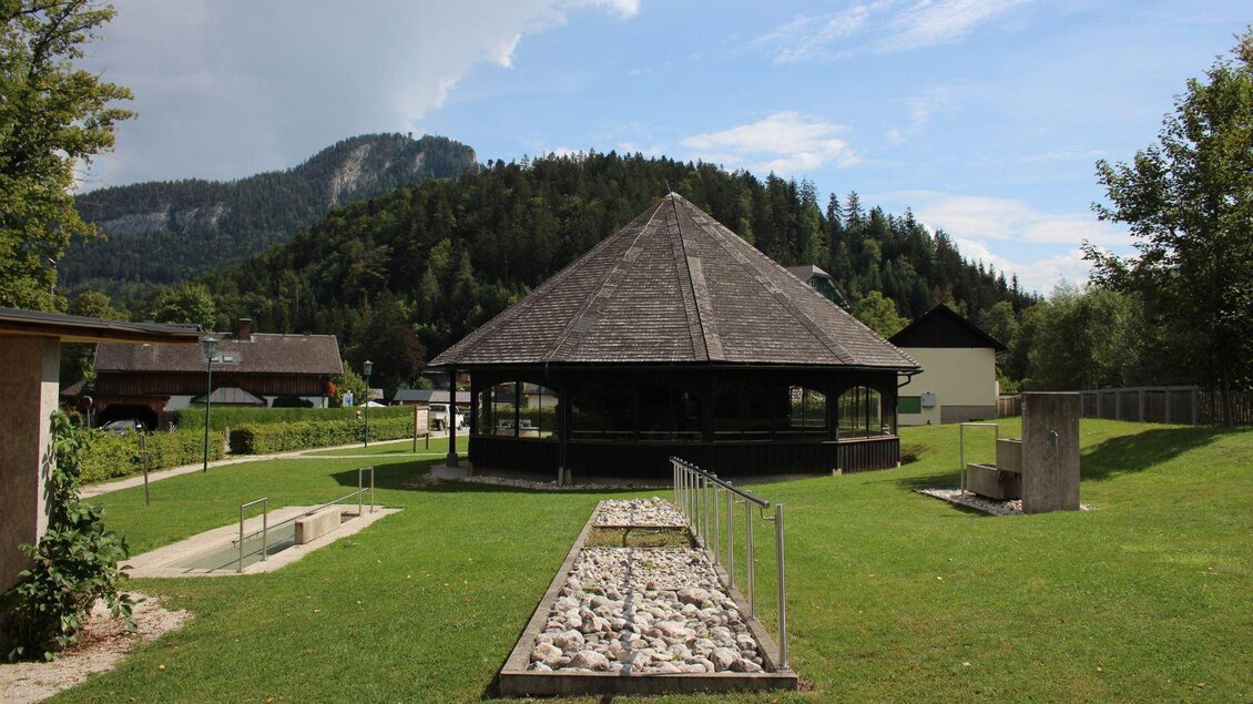 Ein großzügiger grüner Park mit einem runden Pavillon und einem Berg im Hintergrund. Die saftige Wiese ist gut gepflegt und lädt zum Verweilen ein. | © Viola Lechner