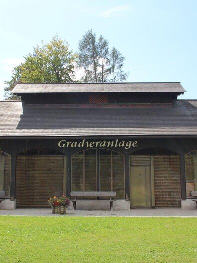 Ein Gebäude mit einem modernen Holzdesign und großen Fenstern. Es steht in einer grünen Umgebung mit Bäumen und einer gepflegten Rasenfläche. | © Viola Lechner