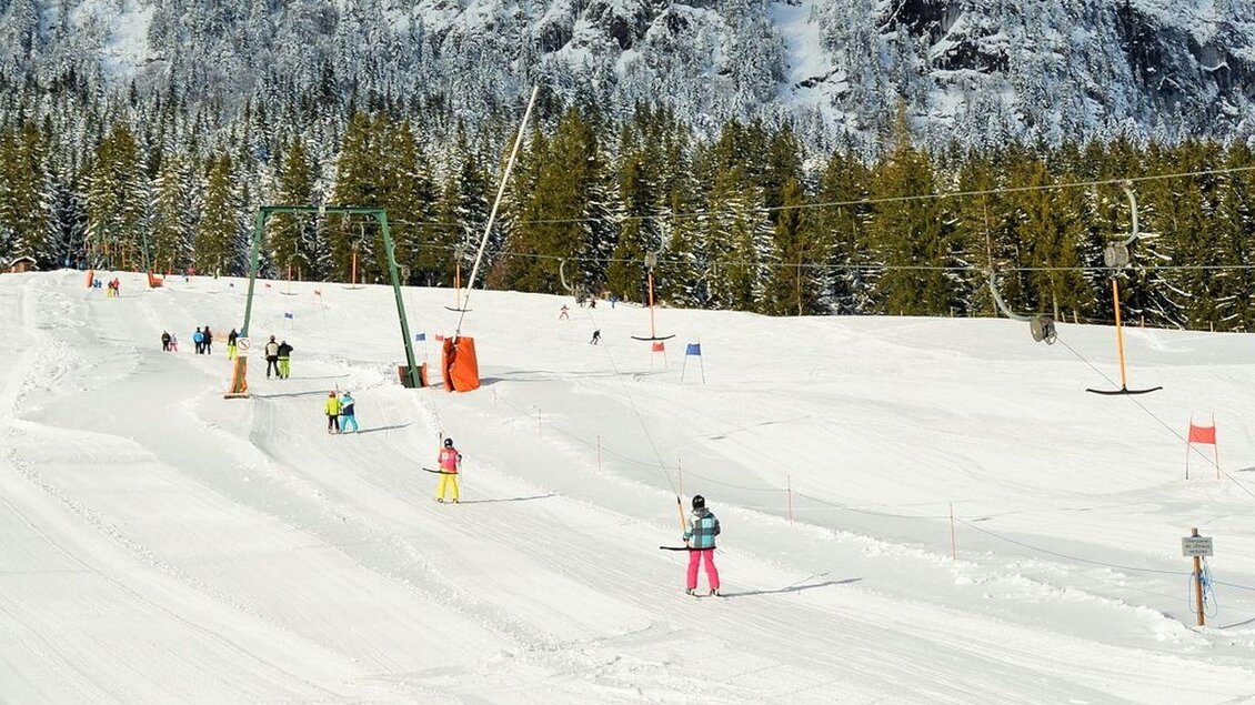 <p>Eine schneebedeckte Skipiste mit Skifahrern und dem Grafenwiesenlift im Hintergrund. Die Landschaf in Tauplitz ist mit frischem Scnee bedeckt..</p> | © Thomas Sölkner