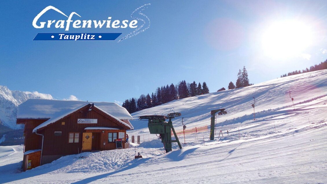 <p>Die Skihütte Grafenwiese ist direkt neben dem gleichnamigen Skilift gelegen. Die Sonne scheint über die verschneite Umgebung in Tauplitz.</p> | © Grafenwiese Tauplitz