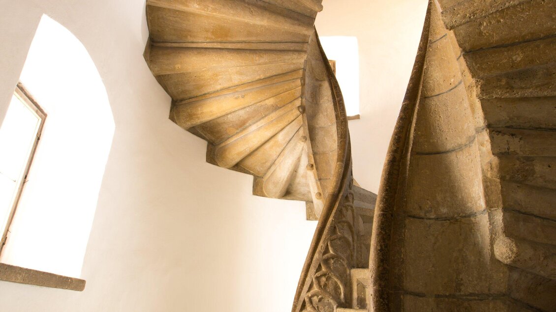 Eine elegante, geschwungene Treppe aus Stein. Das Licht fällt sanft durch die Fenster und hebt die Struktur der Treppe hervor. | © Graz Tourismus - Harry Schiffer