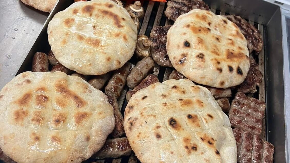 Gegrilltes Fleisch und frisches Fladenbrot auf einem Grill. Neben dem Essen liegen rote Paprikaschoten.