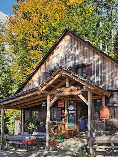 A picturesque wooden cabin, surrounded by colorful autumn leaves. The wooden porch and benches invite you to relax. | © Grimminghütte