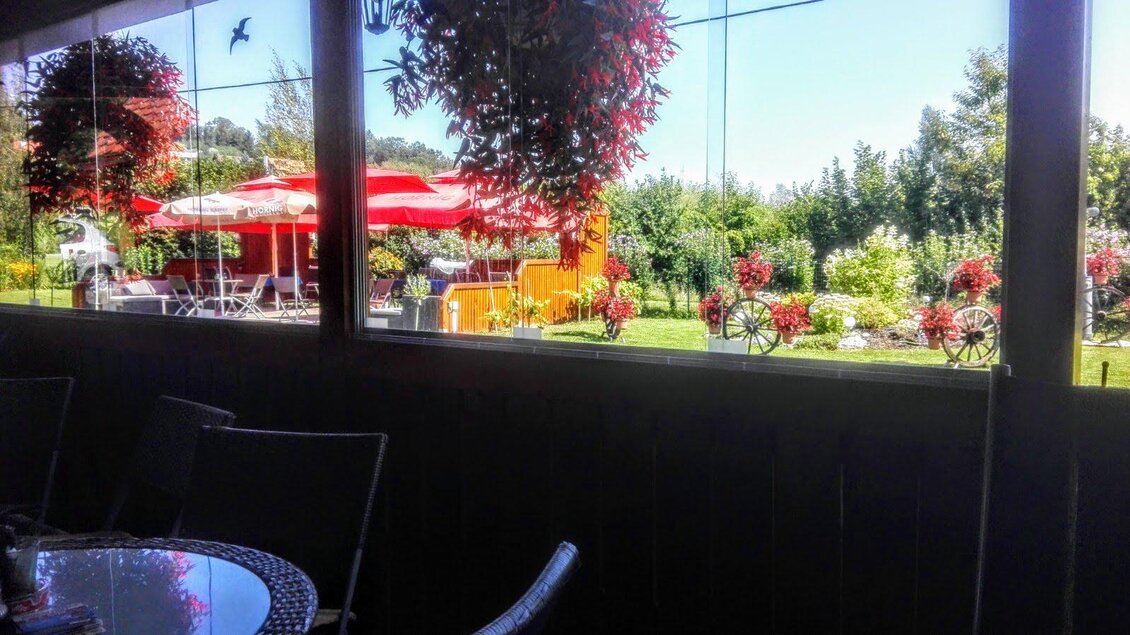 Ein schöner Garten mit bunten Blumen und einer Terrasse mit roten Sonnenschirmen. Im Hintergrund sind grüne Bäume und strahlend blauer Himmel sichtbar. | © Grottenhofer Stub´n