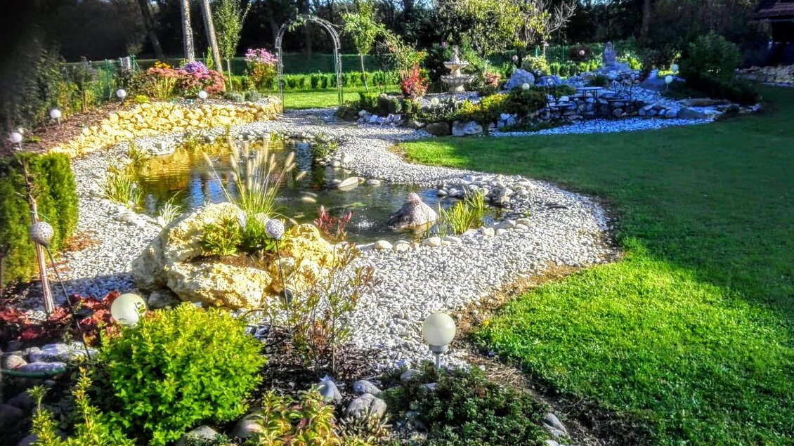 Ein schöner Garten mit einem Teich und vielen bunten Pflanzen. Steinwege und Rasenflächen schaffen eine einladende Atmosphäre. | © Grottenhofer Stub´n