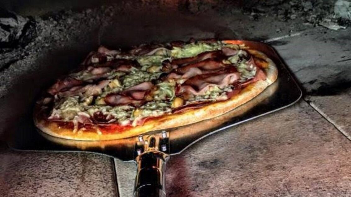 Eine Pizza wird in einem Holzofen gebacken. Flammen sind sichtbar, die eine gemütliche Atmosphäre schaffen. | © Grottenhofer Stub´n