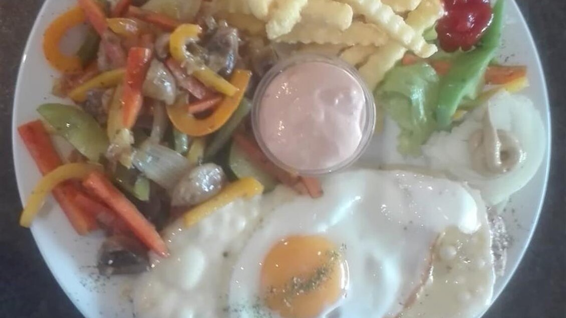 Ein Teller mit zwei Spiegeleiern, Pommes frites, einem Salat und einer bunten Gemüsebeilage. Das Gericht wird mit einer Sauce serviert. | © Grottenhofer Stub´n