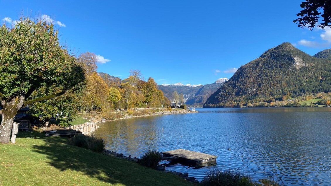 Die ruhige Landschaft von Grundlsee im Ausseerland Salzkammergut mit dem klaren, gleichnamigen See und grünen Wiesen. Im Hintergrund sind die Ausläufer des Toten Gebirges und ein blauer Himmel sichtbar. | © Bettina Scheck