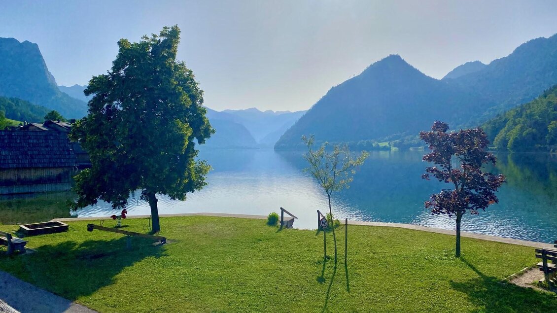 Der ruhige Grundlsee beim Badeplatz Seeklause am Anfang des Sees. Im Hintergrund sind die Ausläufer des Toten Gebirges zu sehen. Grüne Wiesen und Bäume am Ufer schaffen eine friedliche Atmosphäre. | © Bettina Scheck