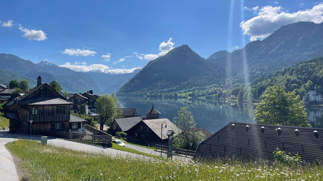 Die malerische Landschaft von Grundlsee mit traditionellen Ausseer Holzhäusern am Ufer des Grundlsees. Im Hintergrund erheben sich die auslaufenden Berge des Toten Gebirges unter blauem Himmel, des Berg Ressen ist prominent im Bild zu sehen. | © TVB Ausseerland/Bettina Scheck