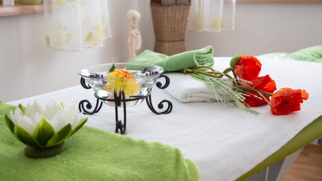 Ein entspannender Massagetisch mit frischen Blumen und Handtüchern in sanften Farben. Das Ambiente ist ruhig und einladend. | © Gsund &amp; fesch 