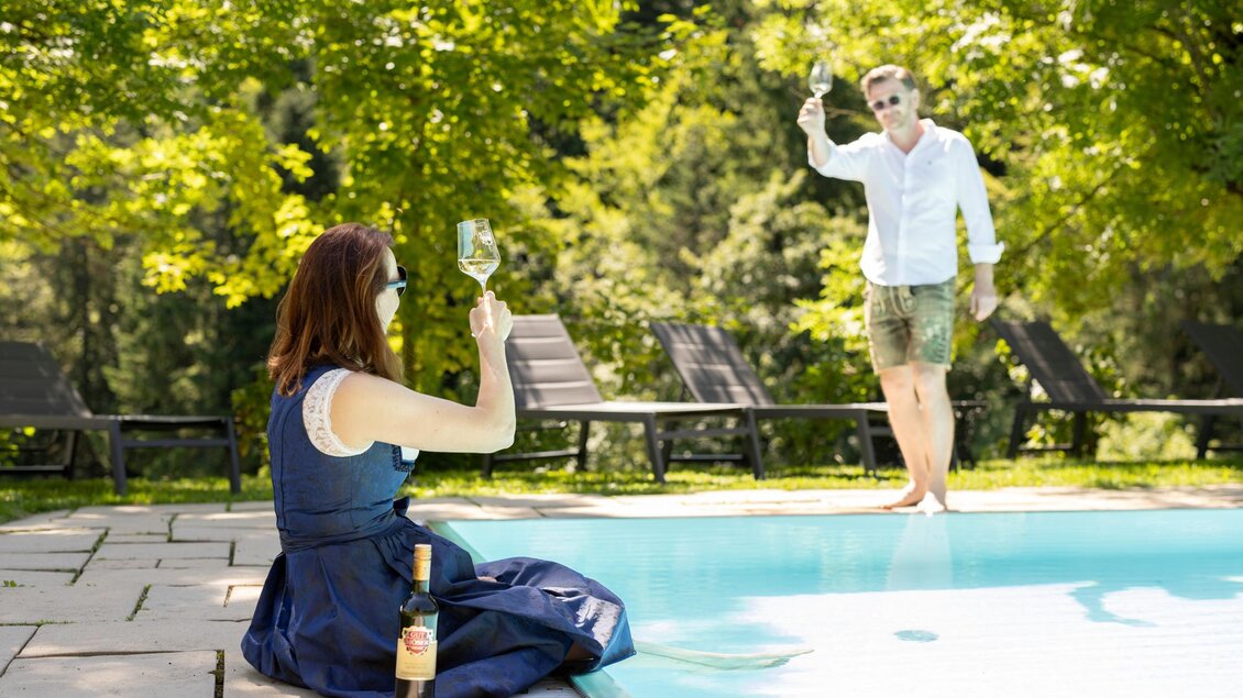 Ein Paar genießt einen entspannten Tag am Pool. Sie stoßen mit Gläsern an, umgeben von grüner Natur. | © Gut Moser