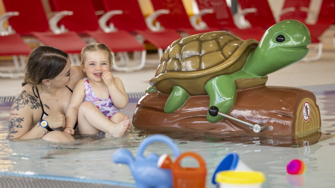Ein Kind und eine Erwachsene verbringen Zeit im Wasser. Neben ihnen steht ein buntes, aufblasbares Schildkröten-Spielzeug. | © H2O-Hoteltherme GmbH
