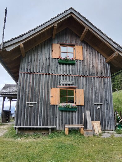 Ein traditionelles Holzhaus mit Holzläden und Fensterkästen. Es ist von einer grünen Wiese umgeben. | © Rinnhofer