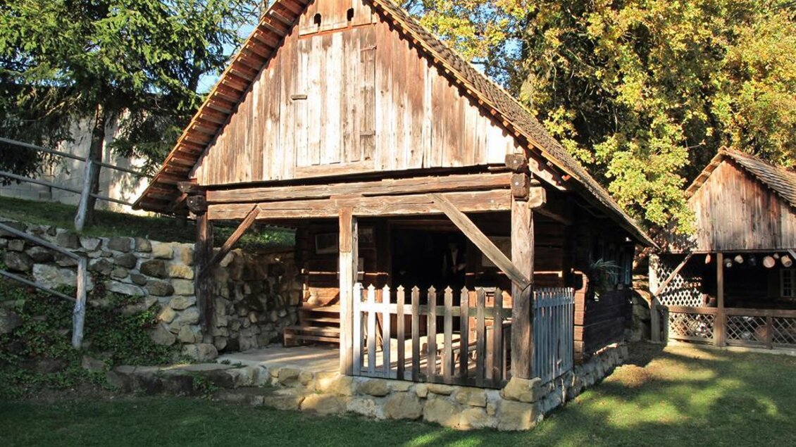Eine rustikale Holzhütte mit einem steilen Dach steht inmitten von Bäumen. Der Garten ist gepflegt und mit Rasenflächen umgeben. | © Gemeinde St. Veit in der Südsteiermark