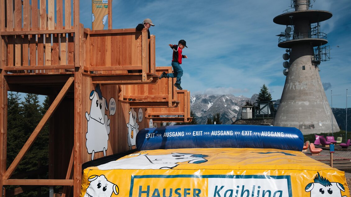 Kind springt vom Schaf-Sprungturm auf ein Luftkissen. | © Hauser Kaibling