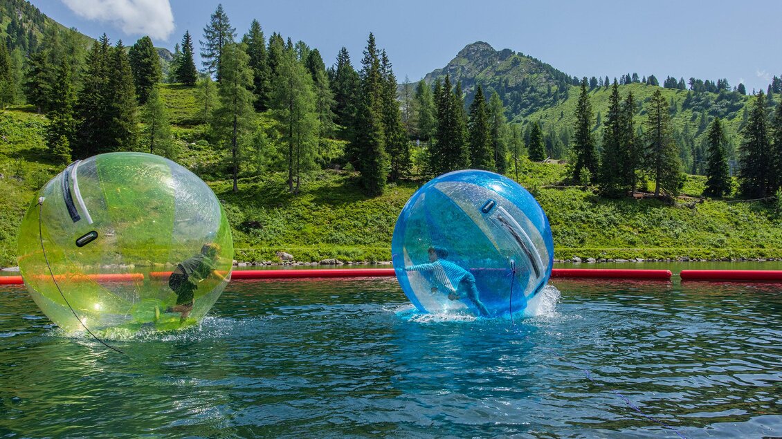 Kinder laufen in Wasserbällen über einen Bergsee. | © Rene Eduard Perhab