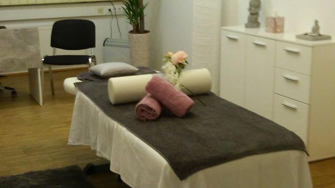 Ein ruhiger Massagebereich mit einem Behandlungstisch, dekoriert mit Handtüchern und Blumen. Pflanzen und ein grauer Teppich sorgen für eine entspannte Atmosphäre. | © Miriam Zamberger