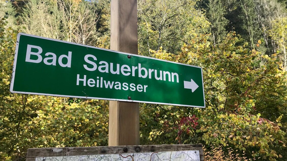 Ein Wegweiser zeigt den Weg nach Bad Sauerbrunn. Im Hintergrund sind bunte Bäume und eine grüne Landschaft zu sehen. | © TV Südsteiermark