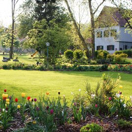 Ein schöner Garten mit bunten Blumen und einer Skulptur. Im Hintergrund ist ein charmantes Haus und viel Grün zu sehen. | © Tourismusverband Oststeiermark