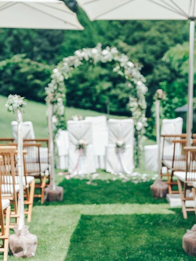 An elegant outdoor wedding ceremony with wooden benches and a beautifully decorated altar. The surroundings are green and inviting, perfect for a special day. | © RETTER Bio-Naur-Resort