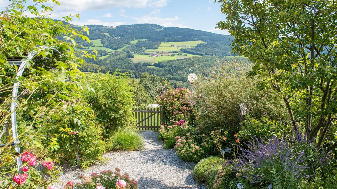 Ein schöner Garten mit bunten Blumen und einem Kiesweg. Im Hintergrund sind Hügel und ein klarer Himmel zu sehen. | © Helmut Schweighofer