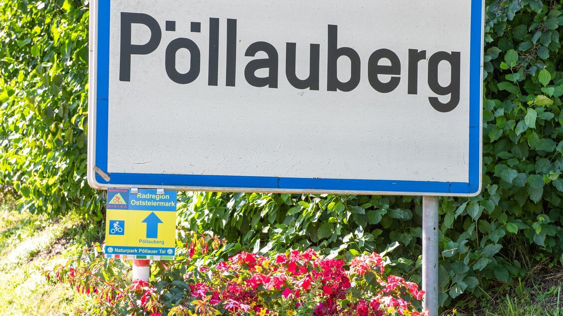 Ein Schild mit dem Ortsschild „Pöllauberg“ steht umgeben von bunten Blumen. Es zeigt den Eingang zu der Gemeinde. | © Helmut Schweighofer