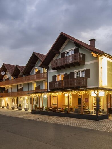 Ein charmantes Hotelgebäude mit Holzverkleidung und Balkon. Die Fassade ist bei Dämmerung beleuchtet und lädt zum Verweilen ein. | © (c) Bachner Hotelbetriebsges.m.b.H.