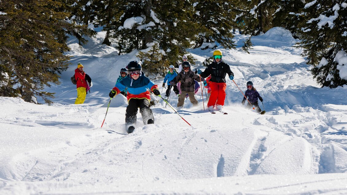Eine Gruppe von Skifahrern fährt durch eine schneebedeckte Landschaft. Die Sonne scheint und es gibt viele Bäume im Hintergrund. | © Planneralm/Tom Lamm