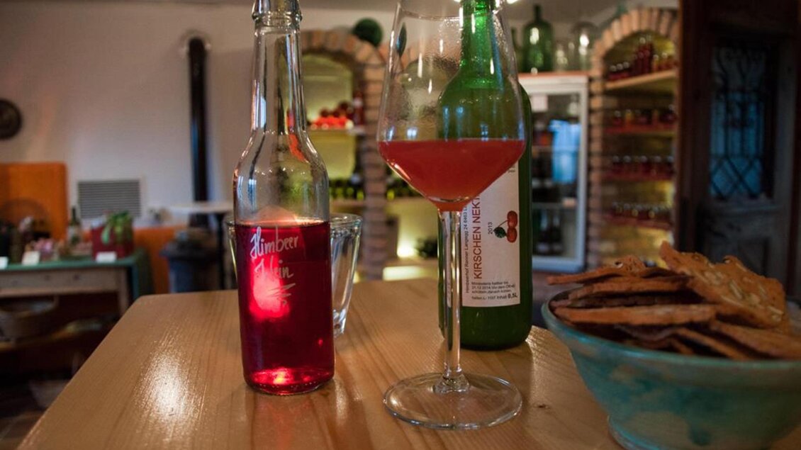 Ein Tisch mit Getränken und einer Schale voller Snacks. Im Vordergrund steht ein Cocktailglas mit rotem Getränk und zwei Flaschen im Hintergrund. | © Susanne Maria Renner-Vracko | Himbeerhof Renner - Vracko
