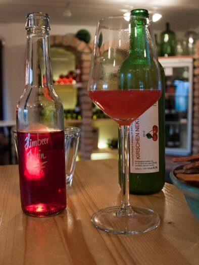 Ein Tisch mit Getränken und einer Schale voller Snacks. Im Vordergrund steht ein Cocktailglas mit rotem Getränk und zwei Flaschen im Hintergrund. | © Susanne Maria Renner-Vracko | Himbeerhof Renner - Vracko