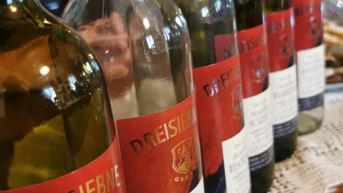 Eine Reihe von Weinflaschen mit roten Etiketten steht auf einem Tisch. Die Flaschen sind teilweise leer und zeigen ein geselliges Ambiente. | © Susanne Maria Renner-Vracko | Himbeerhof Renner - Vracko