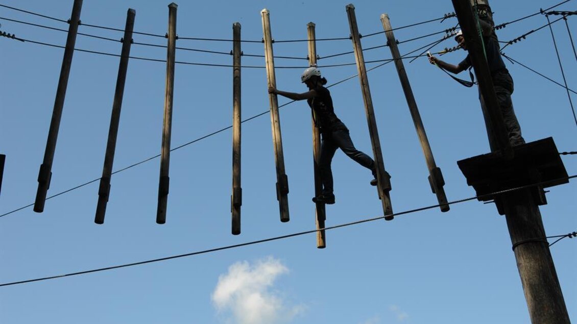 Eine Person balanciert auf einer langen Holzlatte zwischen zwei Pfosten. Der Himmel ist blau mit einigen Wolken. | © Freelife Outdoorsport GmbH