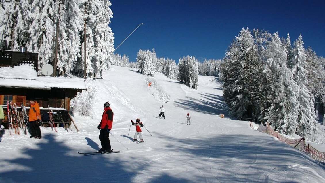 Eine schneebedeckte Piste mit Skifahrern und einem klaren blauen Himmel. Im Hintergrund sind Bäume zu sehen. | © Andreas Schwengerer