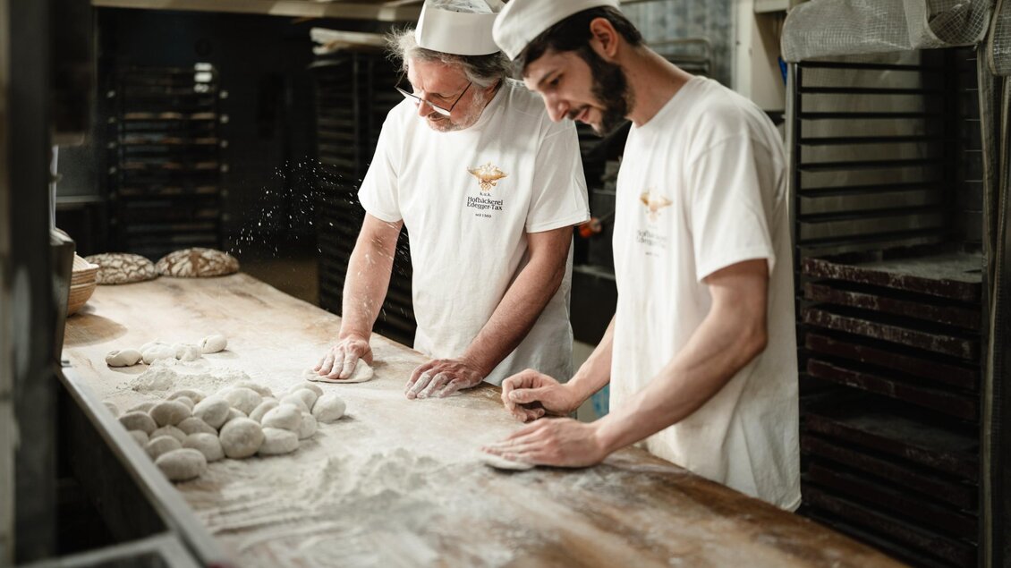 Zwei Bäcker formen in der Hofbäckerei Edegger-Tax Teigstücke von Hand auf einer bemehlten Arbeitsfläche. | © Bernd Grosseck