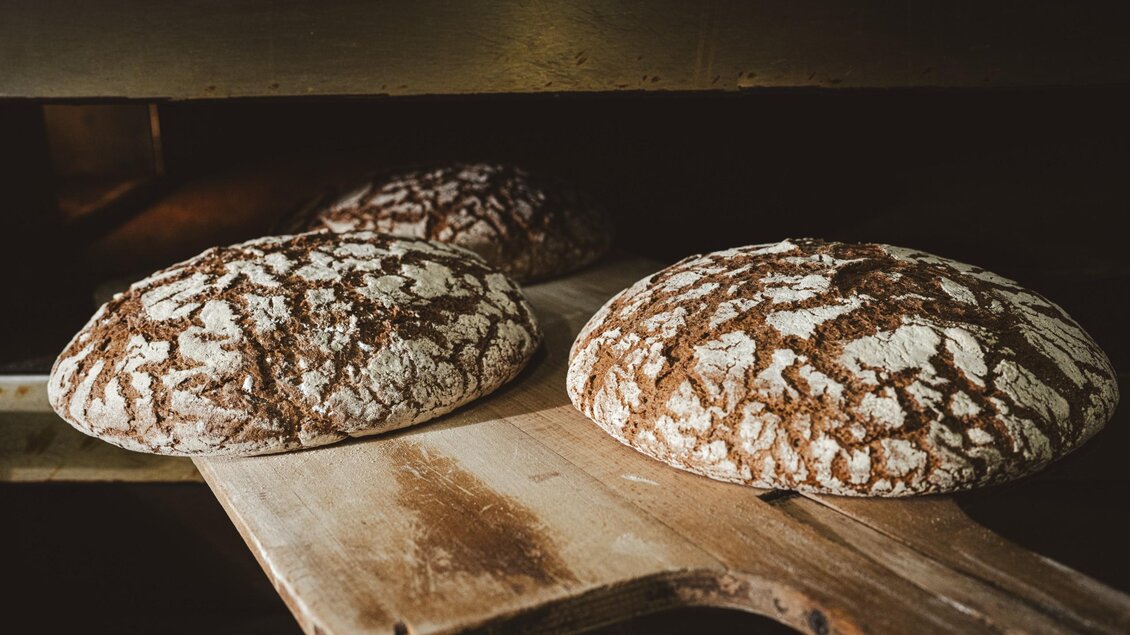 Mehrere Brotlaibe werden mit einem hölzernen Brotschieber aus dem Ofen der Hofbäckerei Edegger-Tax geholt. | © Bernd Grosseck