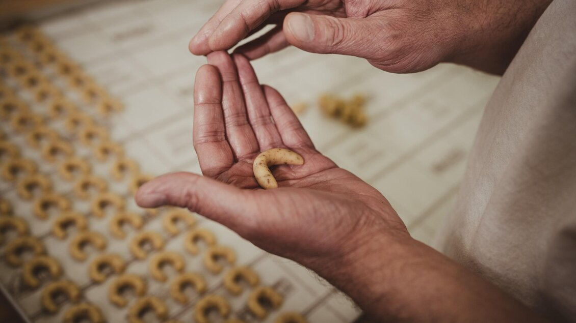 Ein Bäcker formt ein Vanillekipferl von Hand, während weitere Kipferl auf der Arbeitsfläche liegen. | © Bernd Grosseck