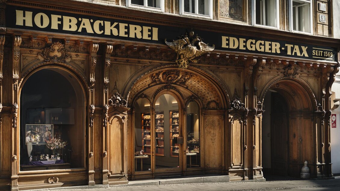Historische Fassade der Hofbäckerei Edegger-Tax mit beleuchteten Schaufenstern und Eingang in Graz. | © Bernd Grosseck