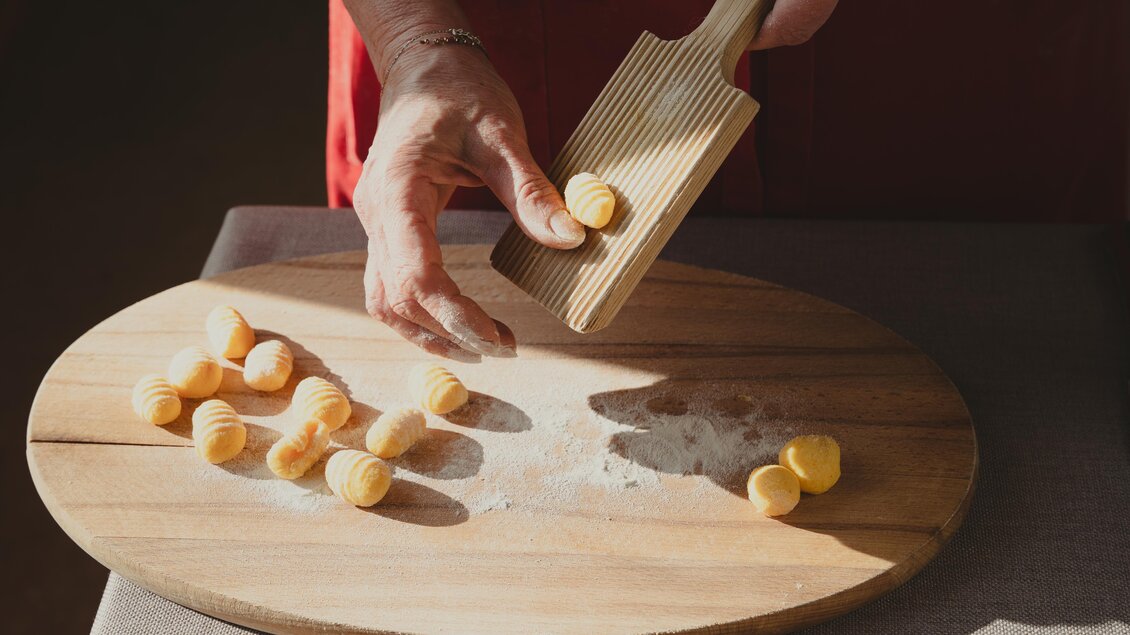 Eine Hand formt Gnocchi auf einer mit Mehl bestäubten Holzplatte in der Hofkuchl des Semriacherhofs. Das Sonnenlicht hebt die handwerkliche Zubereitung hervor. | © Wolfgang Hummer