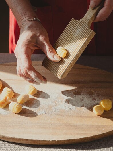 A hand is shaping gnocchi on a floured wooden board in the courtyard kitchen of Semriacherhof. The sunlight highlights the artisanal preparation. | © Wolfgang Hummer