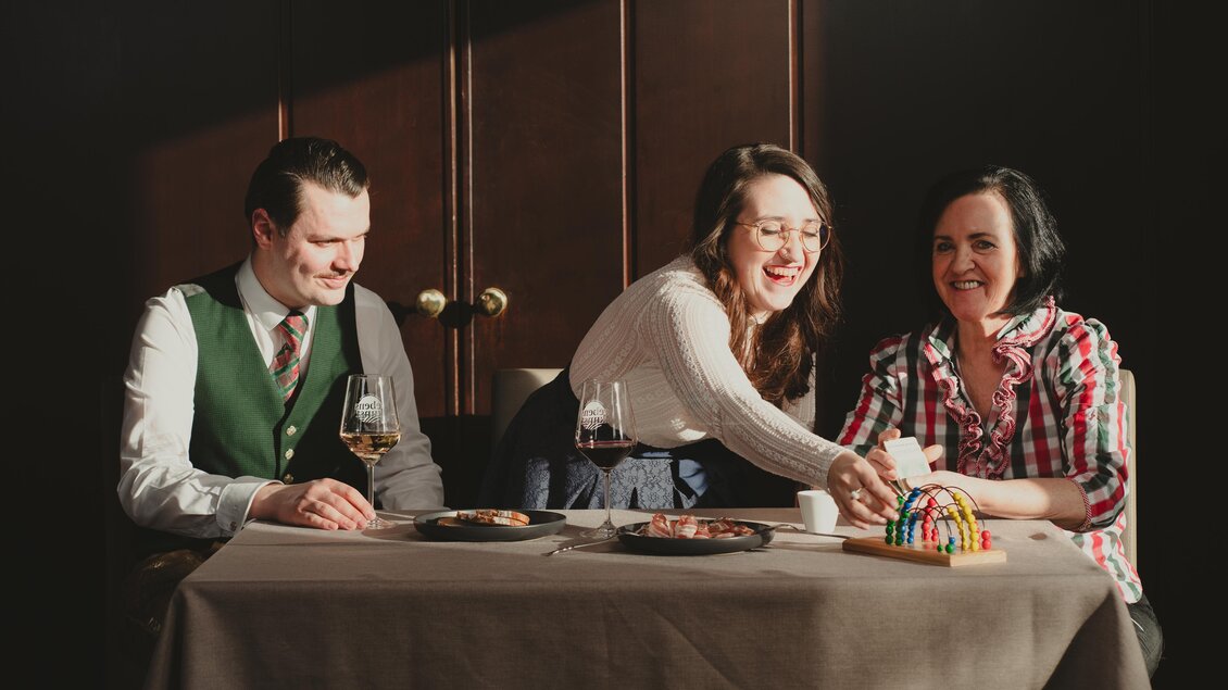 Die Gastgeberfamilie des Semriacherhofs genießt einen entspannten Moment am Tisch, umgeben von gutem Essen und herzlichem Lachen, mit warmem Sonnenlicht im Hintergrund. | © Wolfgang Hummer