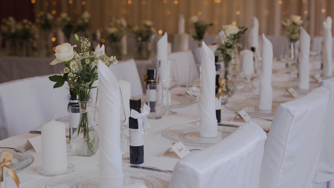 Ein festlich gedeckter Tisch im Semriacherhof, dekoriert mit weißen Servietten, Kerzen, kleinen Flaschen und Blumenarrangements. Die sanfte Beleuchtung sorgt für eine elegante Atmosphäre. | © Wolfgang Hummer