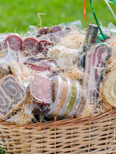 A basket full of various sausage and cheese products, nicely packaged and decorated with hay. The presentation is inviting and delicious. | © Bauernhof König - Familie König