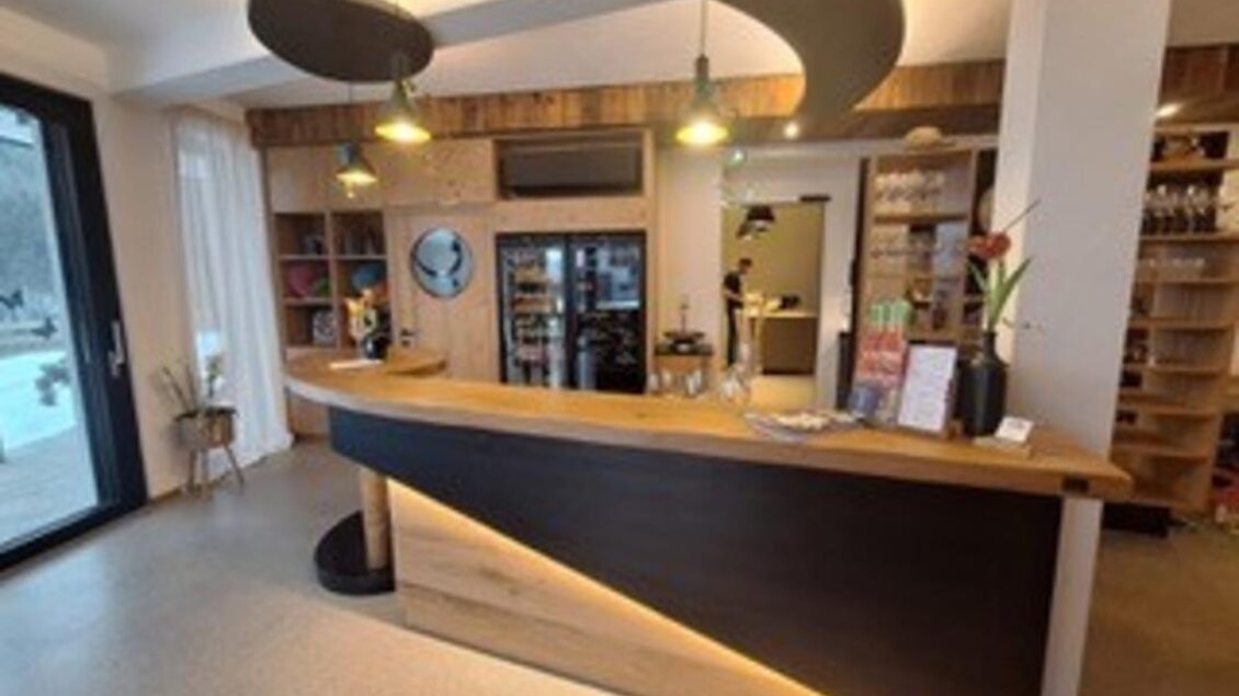 Eine moderne Rezeption mit einem eleganten Holzschreibtisch und warmen Lichtern. Im Hintergrund sind Regale mit verschiedenen Getränken und Snacks zu sehen. | © Fam. Garber