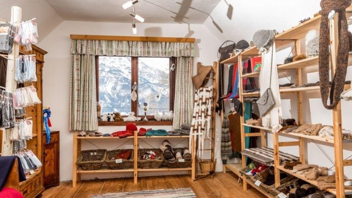 Ein gemütlicher Laden mit Holzregalen, die verschiedene Produkte präsentieren. Durch ein Fenster ist eine Berglandschaft sichtbar. | © Klausnerhof
