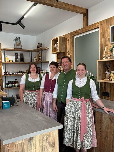 Ein traditioneller Verkaufsraum mit Holzregalen und einem modernen Thekenbereich. Vier Personen in Trachten stehen freundlich posierend im Laden. | © Familie Neukam