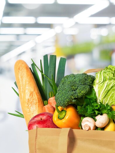 A paper bag full of fresh groceries is lying in a supermarket. Inside, there are vegetables, fruits, and breads. | © shutterstock_402856411