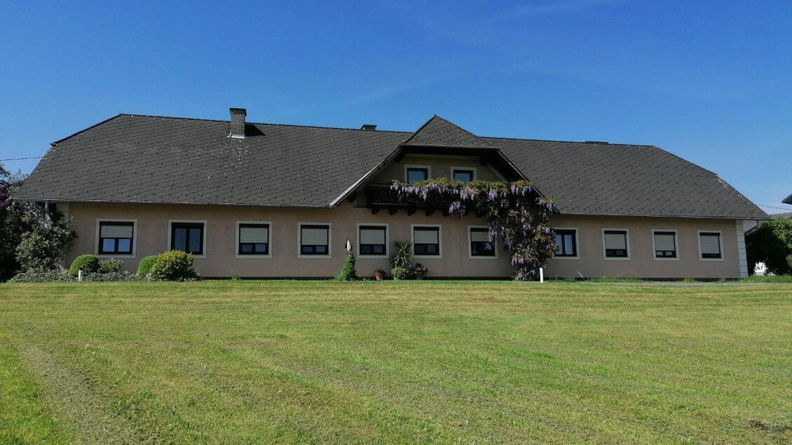 Ein großes, einstöckiges Haus mit einem dunklen Dach und mehreren Fenstern. Der Rasen davor ist gepflegt und grün, umgeben von einigen Pflanzen. | © Familie Stuphann-Jeitler
